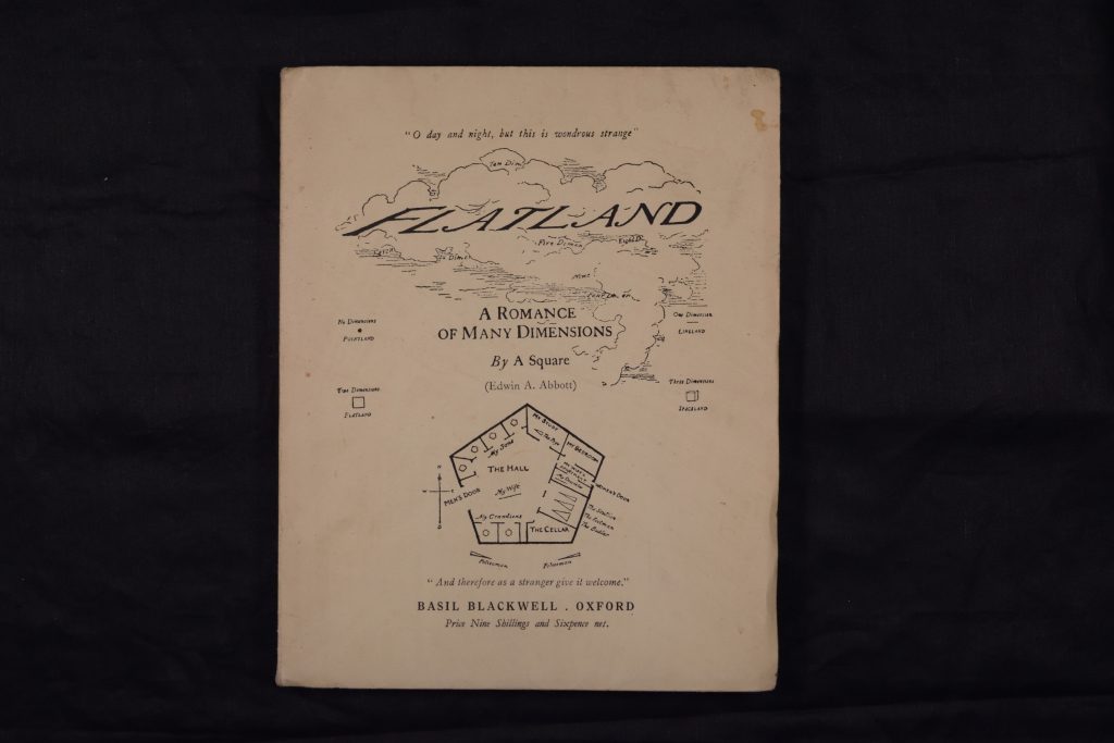 The book 'Flatland: A Romance of Many Dimensions' lying flat so the cover is face-up. The title 'Flatland' has an illustrated cloud around it, and beneath the subtitle there are mathematical diagrams. The cover is printed on a plain beige paper wrapper.