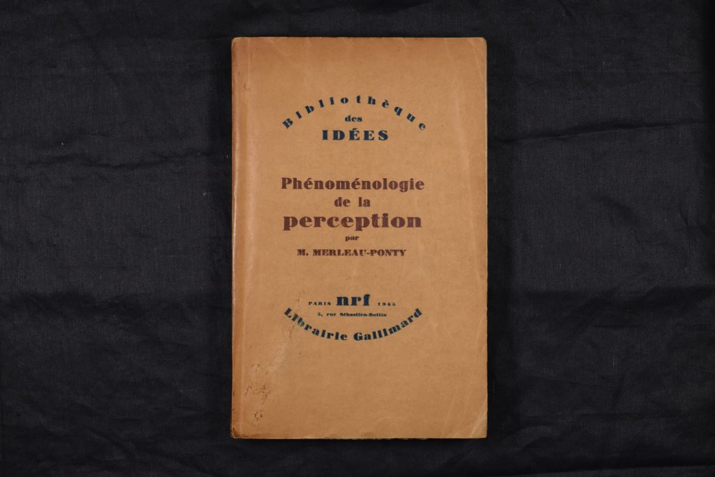 The book 'Phénoménologie de la perception' lying flat so the cover is face-up. The cover is a simple brown paper wrapper, with the title printed in a rounded red roman typeface. Series information and publisher information are at the head and foot of the title respectively, printed in black.