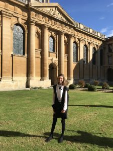 Phoebe's profile photo: she is standing in Front Quad wearing subfusc and holding her mortarboard