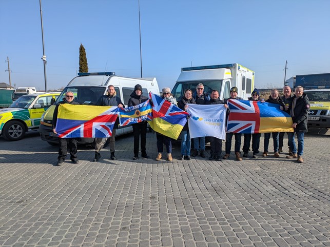The volunteer crew standing in front of the ambulances, holding Union Jack and Ukrainian flags